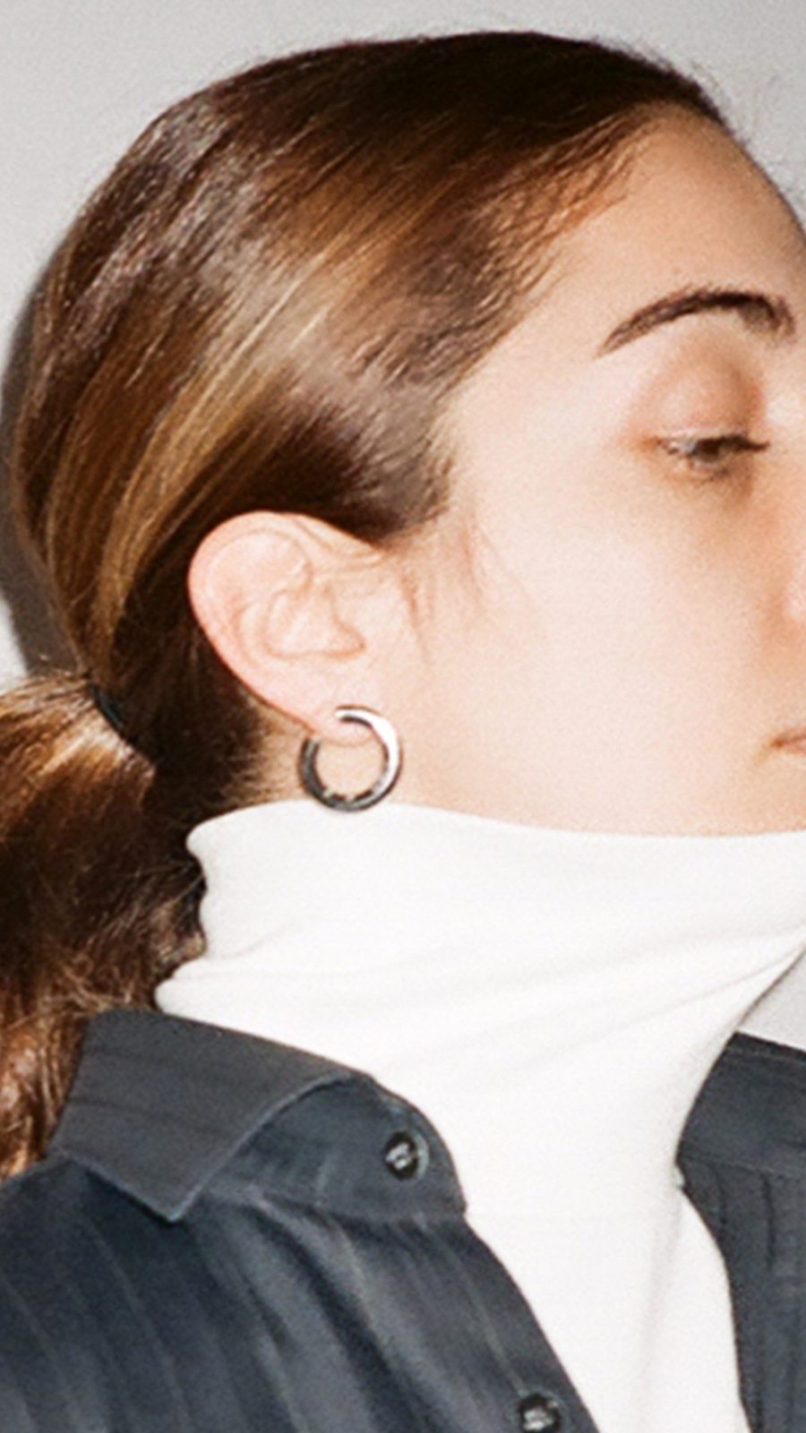 Profile of a model in a white turtleneck with a hoop earring