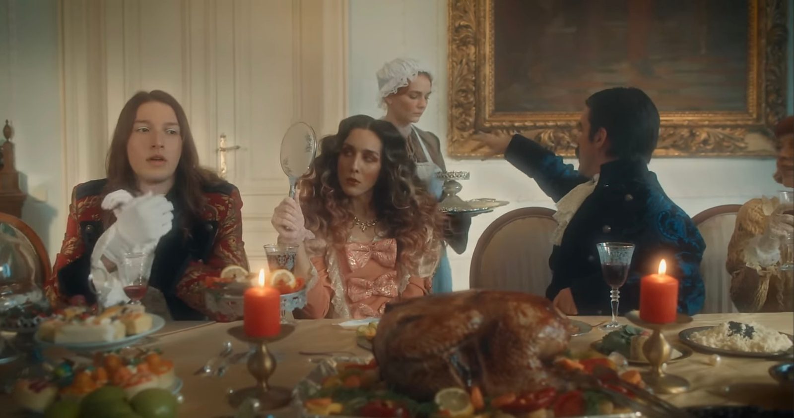 A candlelit banquet scene with guests in period costume, still from the video