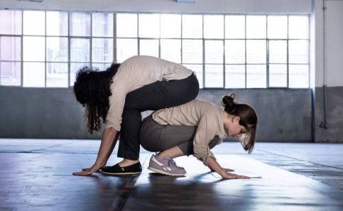 Two performers kneeling face to face beside a laptop on the floor