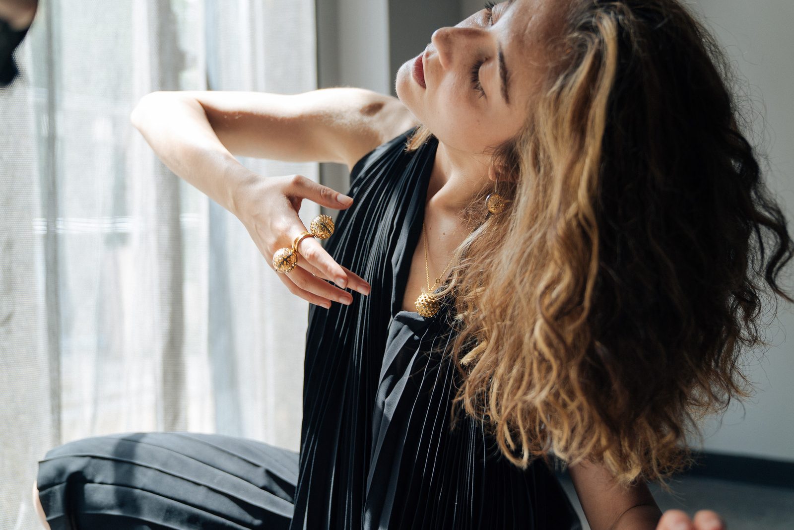 Dila leaning back with a hand at her collarbone
