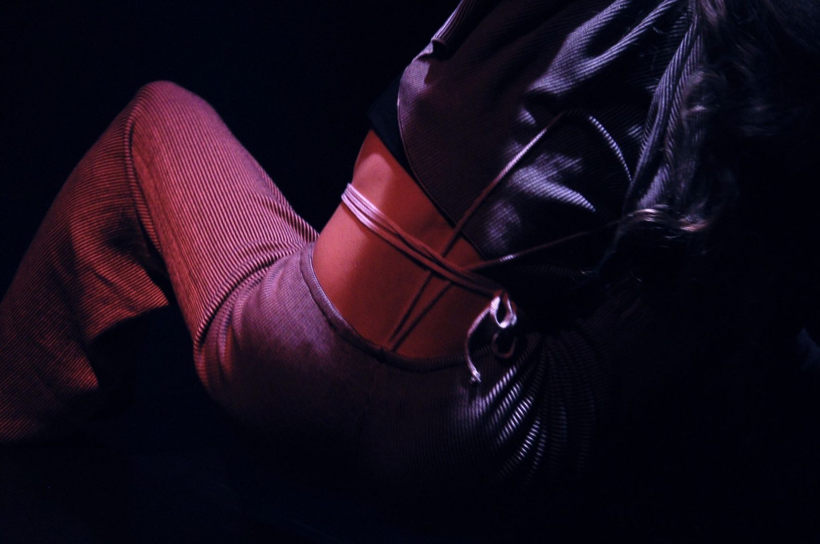 A figure lying back in red and grey under low light