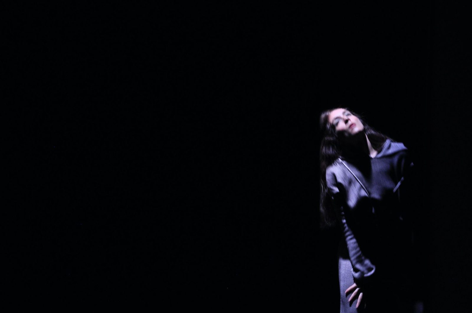 A figure in a dark coat leaning back in near darkness